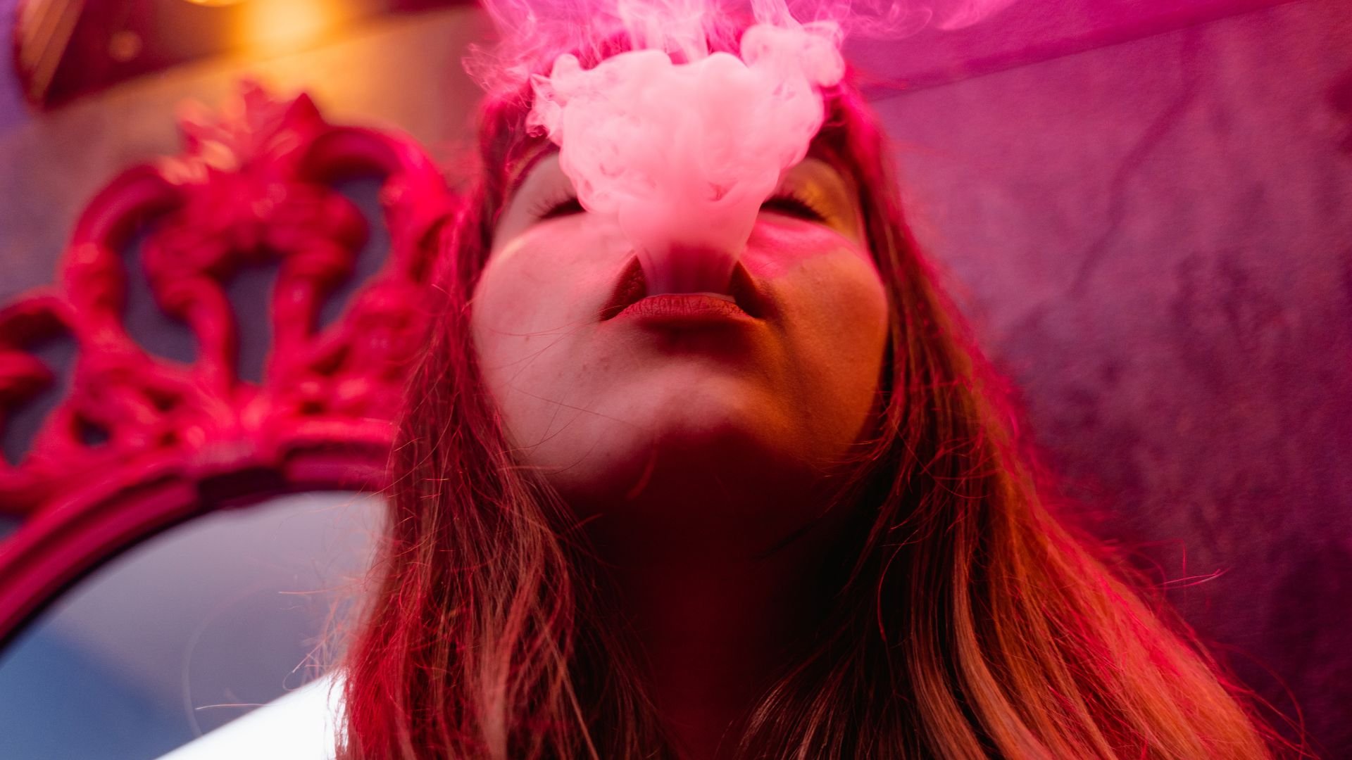 Person blowing pink smoke while wearing a red crown