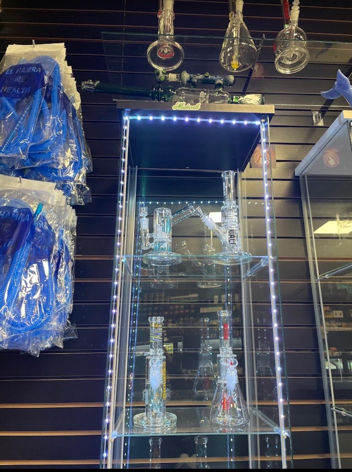 Glass smoking devices displayed in illuminated cabinet with blue bags